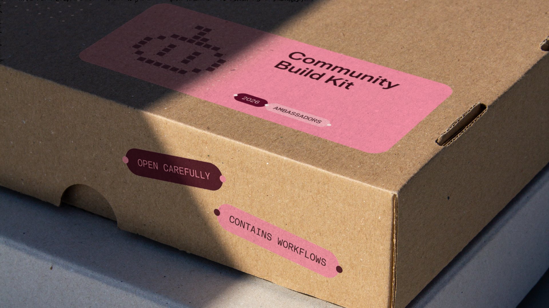 A cardboard “Community Build Kit” box with pink and deep pink stickers